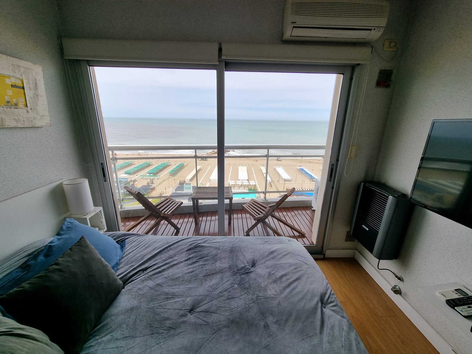 Cama, balcón y vista al mar desde el interior del departamento